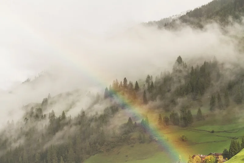 Rainbow over foggy forest and green hills.